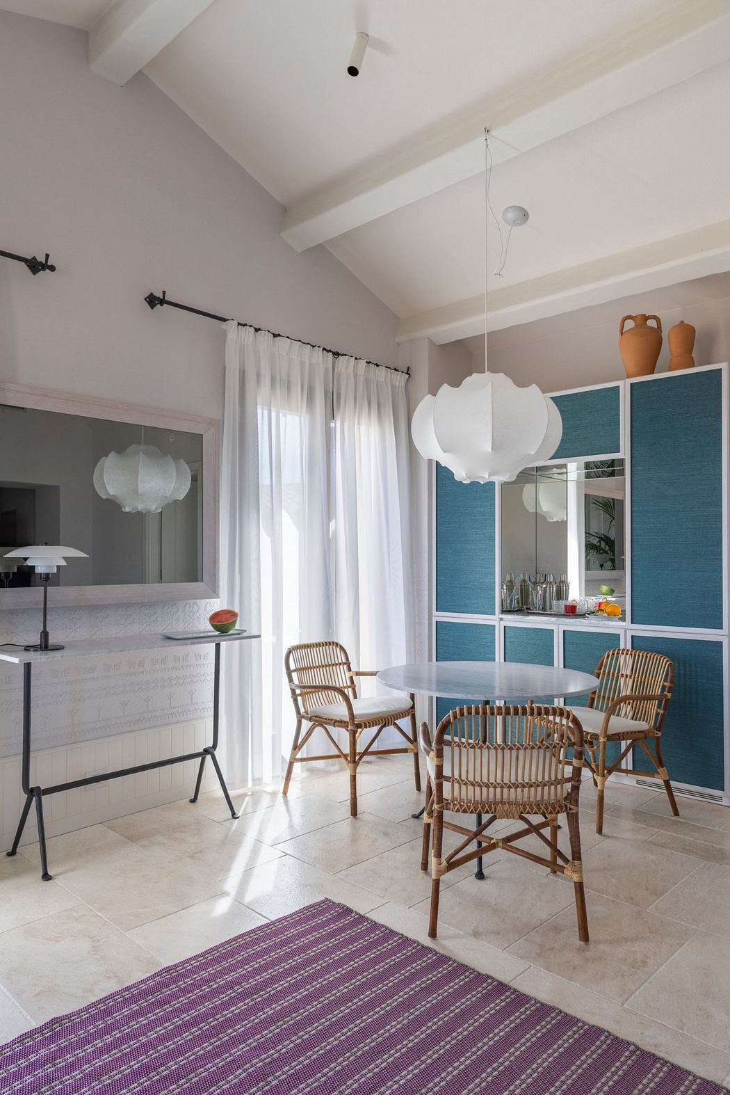 A modern dining area with rattan chairs, white suspended lighting, and blue accent panels.