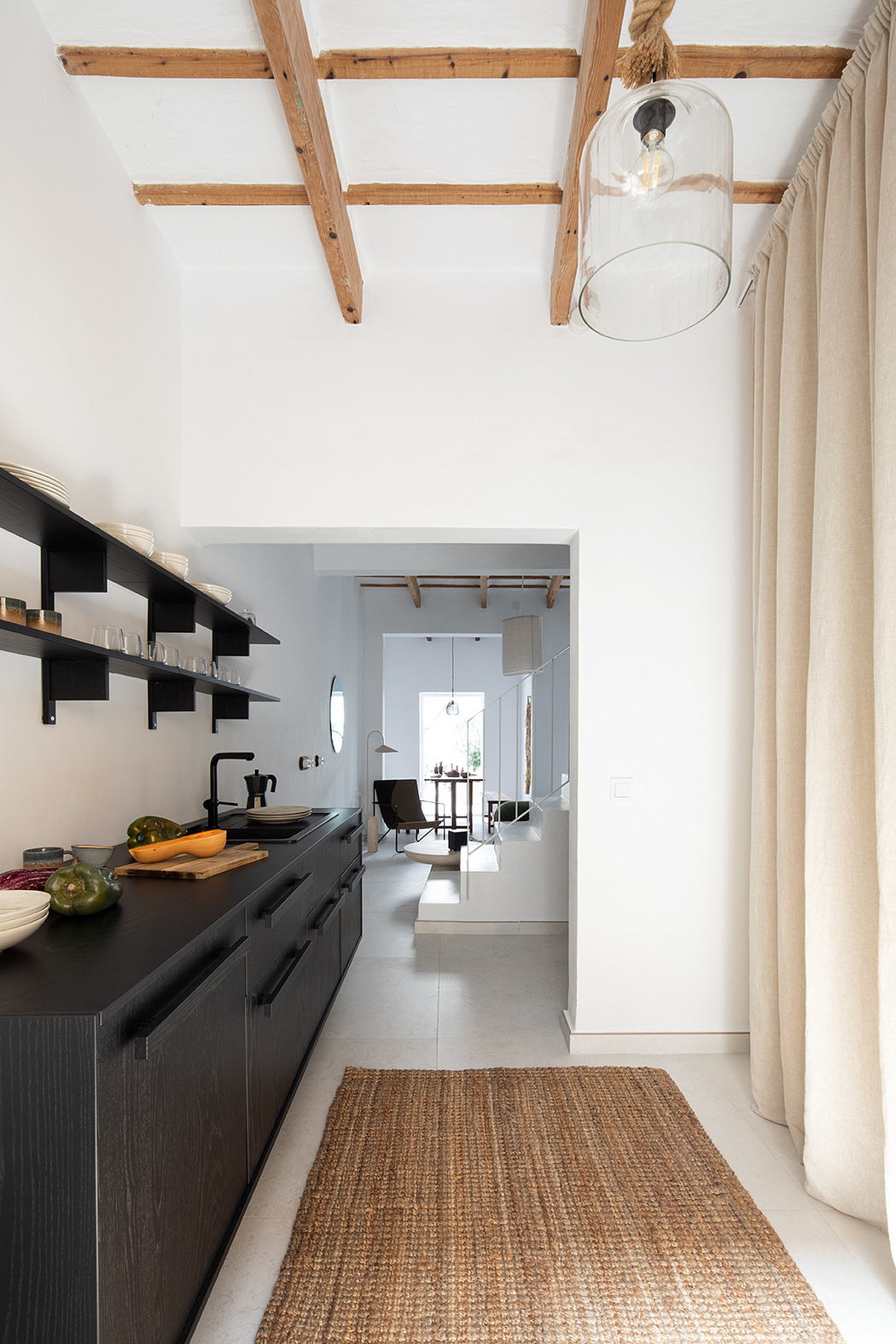 Minimalist kitchen with wood beams, black cabinetry, and a woven area rug.