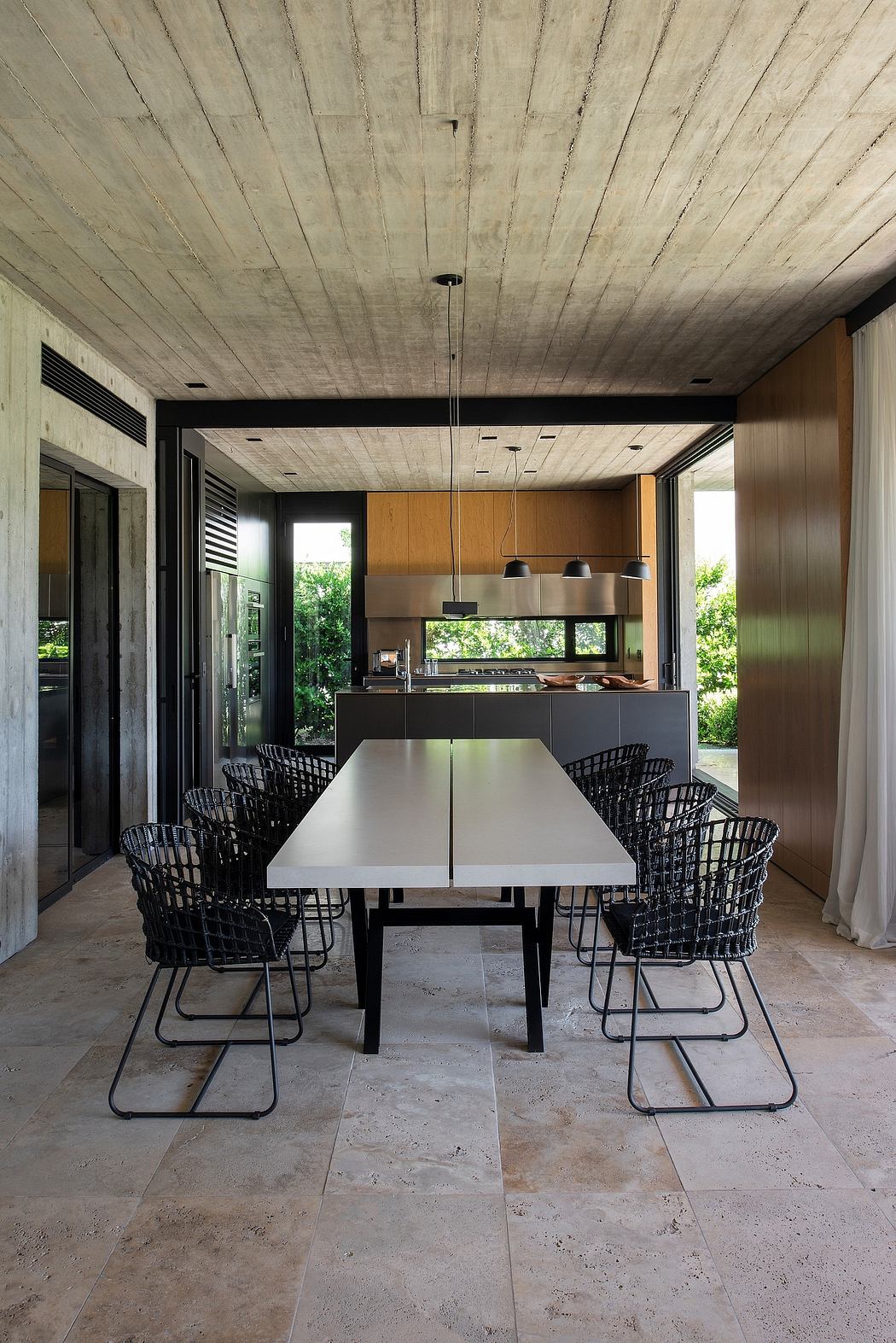 Minimalist dining area with concrete ceiling, metal chairs, and sleek kitchen design.