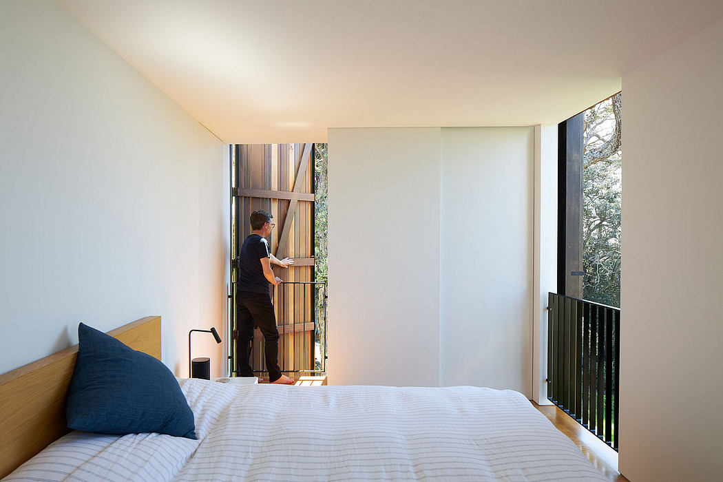 Contemporary bedroom with minimalist design, wooden accents, and a person standing at the balcony.