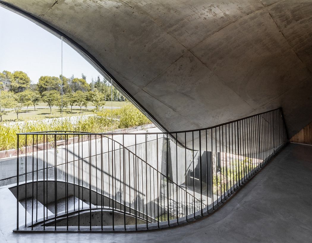 A curved concrete overhang leads to a winding metal railing overlooking a lush landscape.
