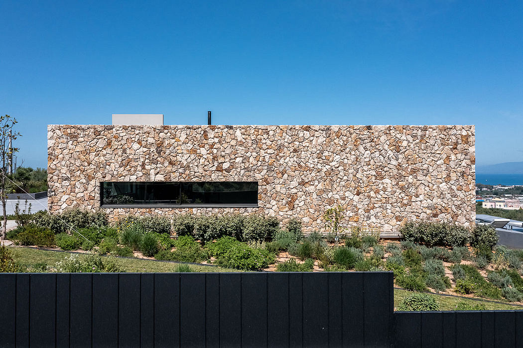 A modern building with a prominent stone wall facade, surrounded by lush greenery.
