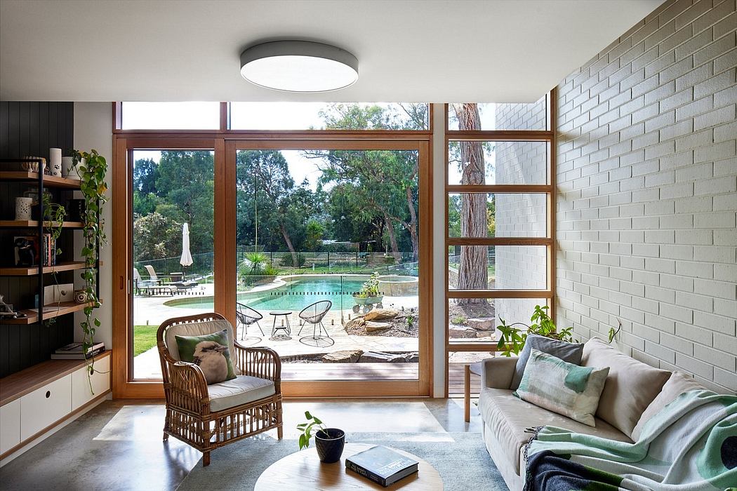 Bright, airy living room with wooden framed windows overlooking a lush outdoor pool area.