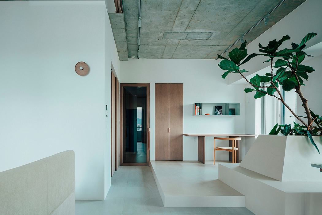 Minimalist interior with exposed concrete ceiling, built-in wood furniture, and potted plant.