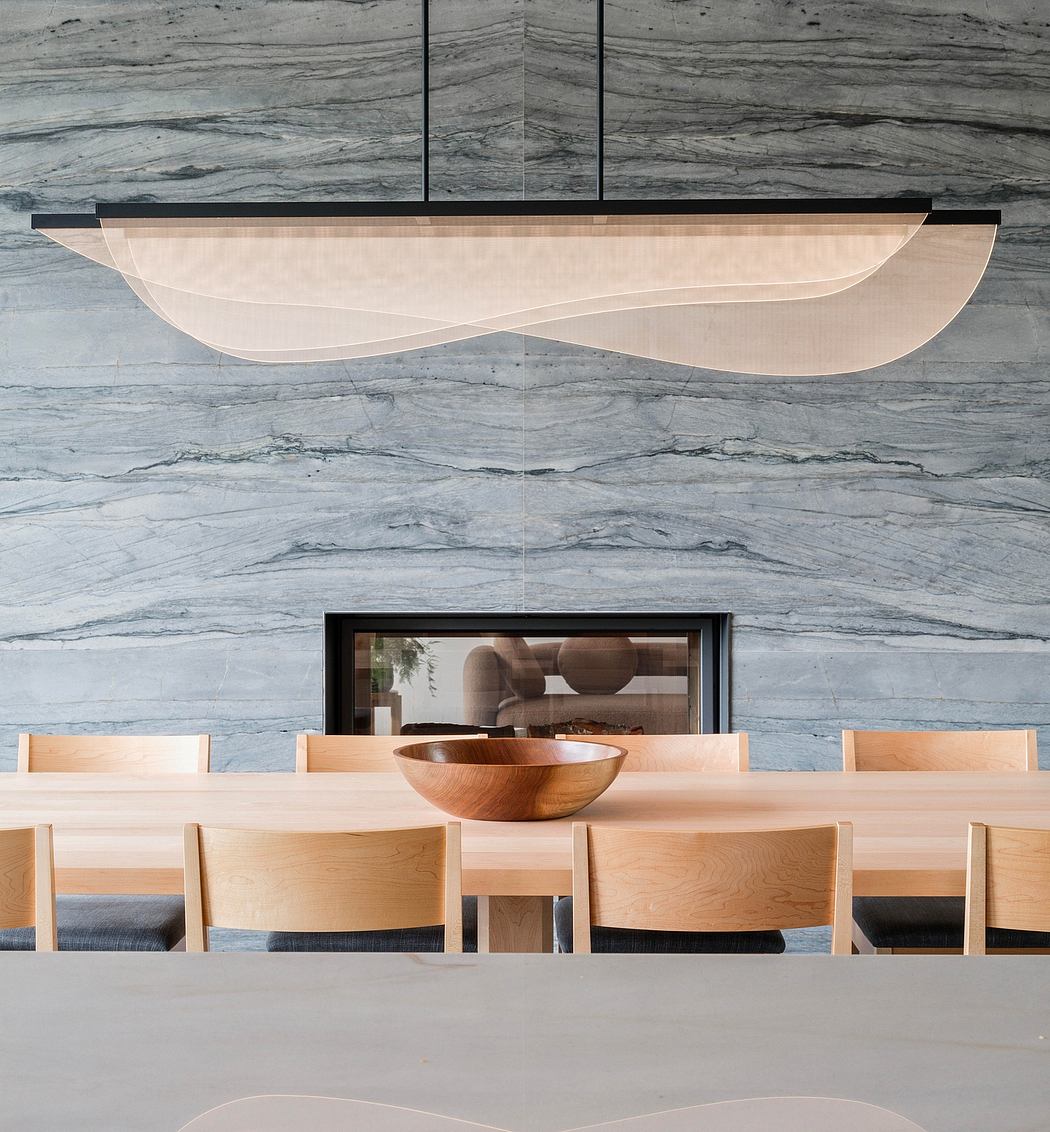Sleek, modern dining room with marble-patterned wall, curved light fixture, and wooden dining set.