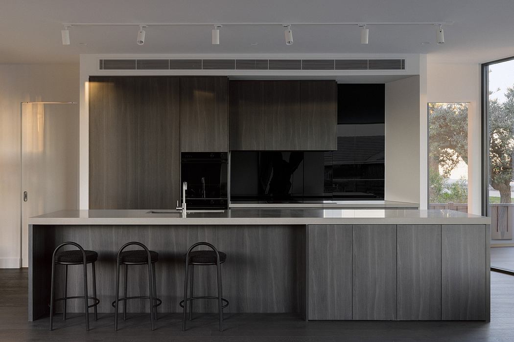 Modern, sleek kitchen with dark wood cabinetry, minimalist black bar stools, and recessed lighting.