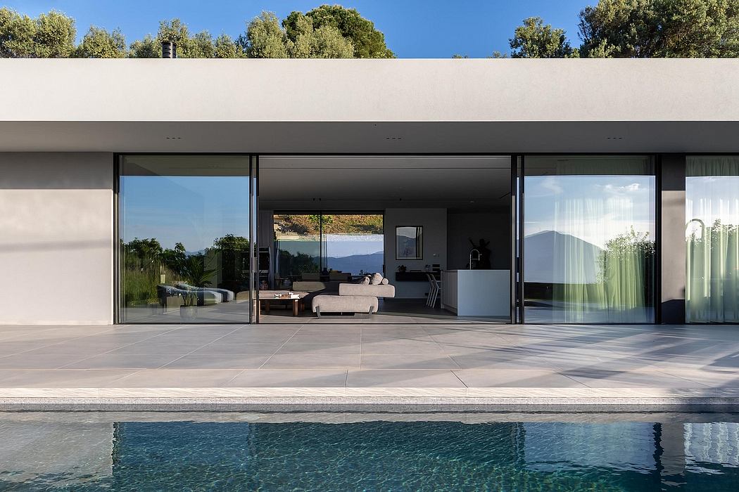 Modern, minimalist villa with expansive glass walls, pool, and outdoor seating area.