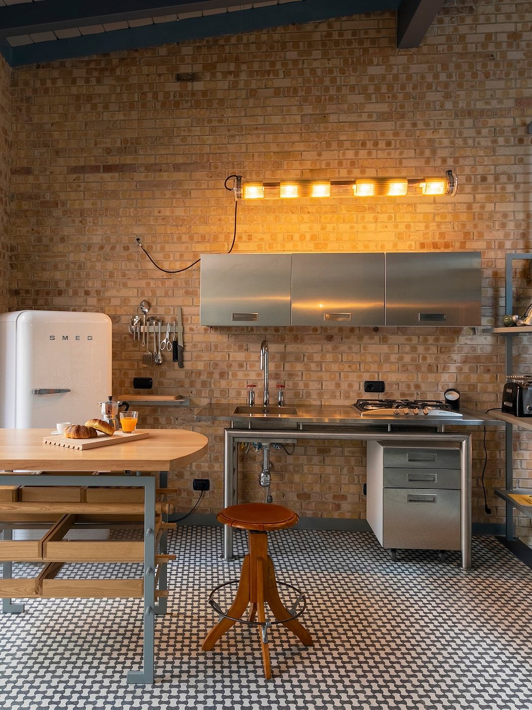 A rustic brick kitchen with a retro-style refrigerator, wood furnishings, and tiled flooring.