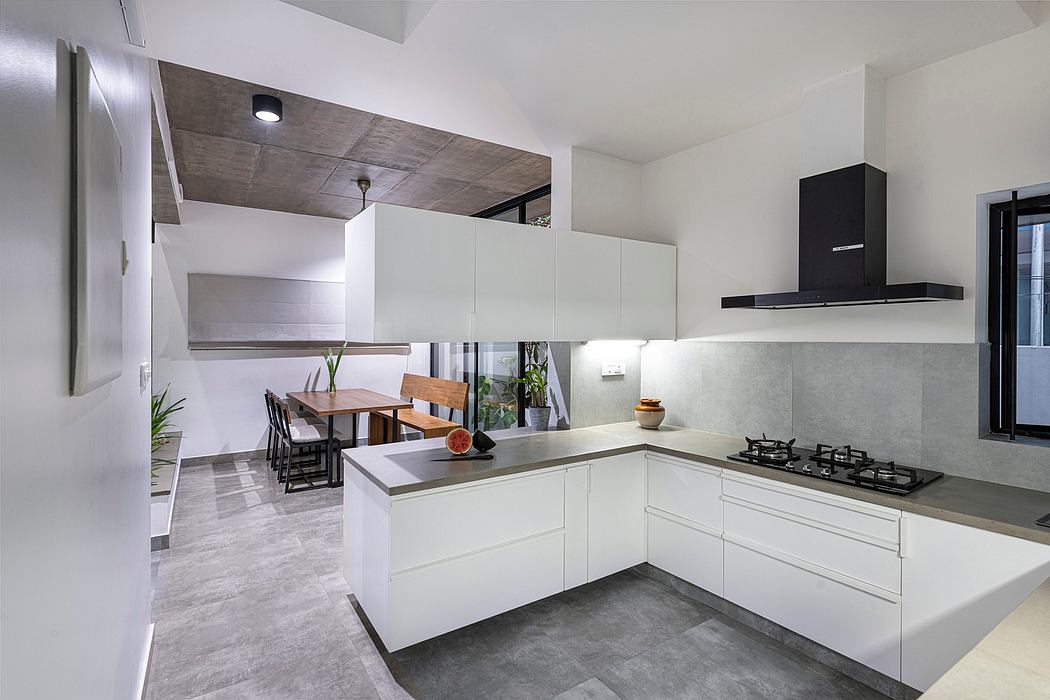 A modern, minimalist kitchen design with white cabinets, black appliances, and concrete flooring.