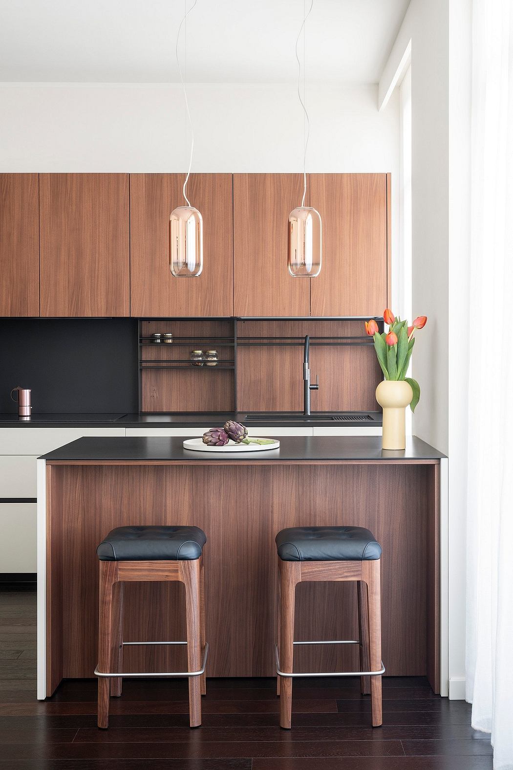 Modern kitchen with sleek wood cabinets, black countertops, and stylish pendant lights.
