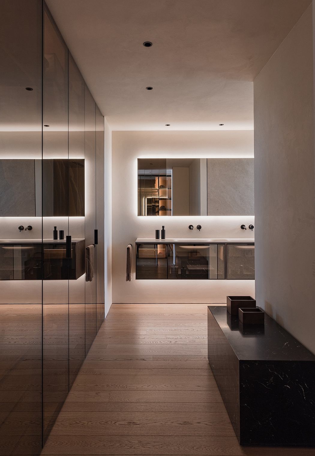 Minimalist bathroom with sleek wooden cabinets, backlit mirrors, and dark stone accents.
