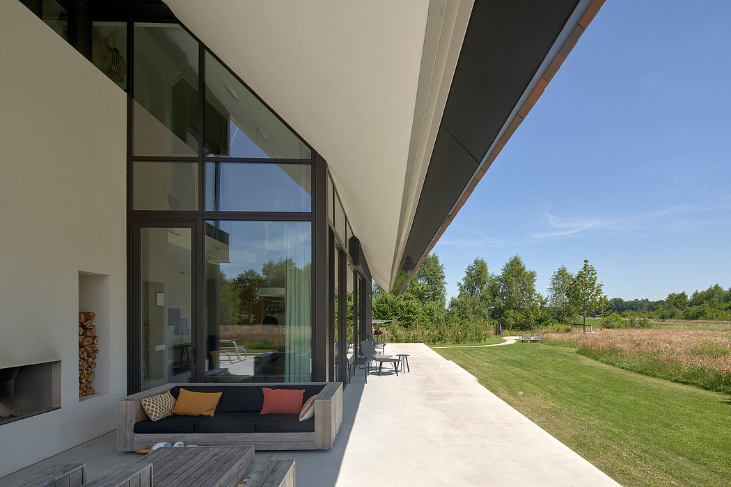 Contemporary open-plan interior with glass walls, outdoor seating, and verdant landscape.