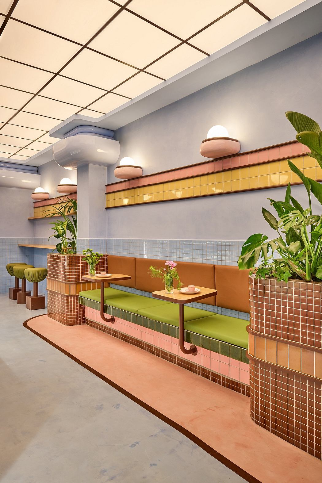 A modern café interior with geometric tile patterns, built-in seating, and lush greenery.
