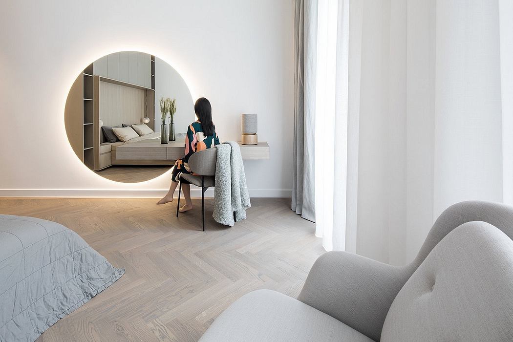 A modern, minimalist bedroom with a circular mirror, plush seating, and natural light.