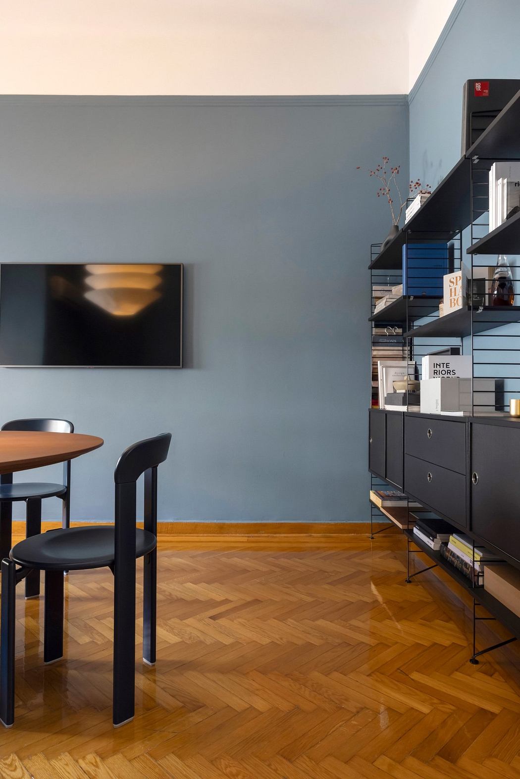 A modern, minimalist interior with a black TV, shelving unit, and wooden floors.