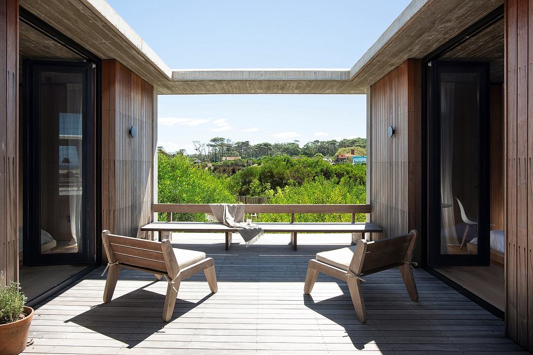 Peaceful outdoor deck with wooden furniture and panoramic forest views through framed windows.