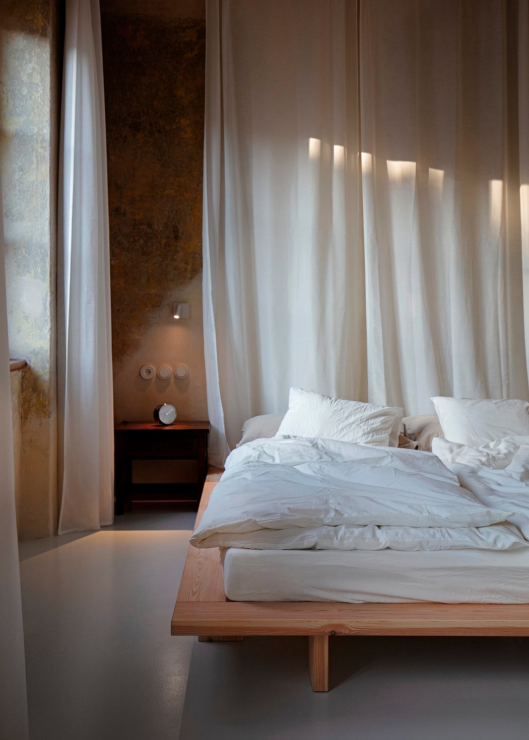 Serene bedroom with white curtains, soft bedding, and wood accents creating a cozy ambiance.