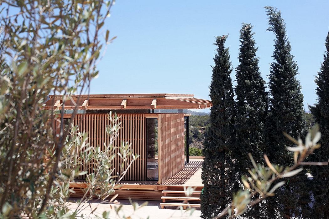 Wooden cabin-like structure with slatted walls and a raised deck, surrounded by pine trees.
