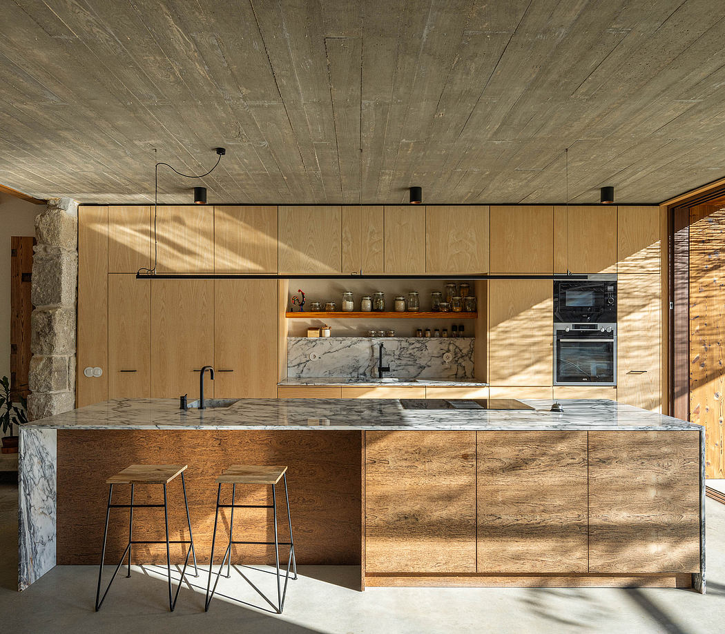 Minimalist kitchen interior with natural wood cabinetry, marble countertops, and industrial lighting.