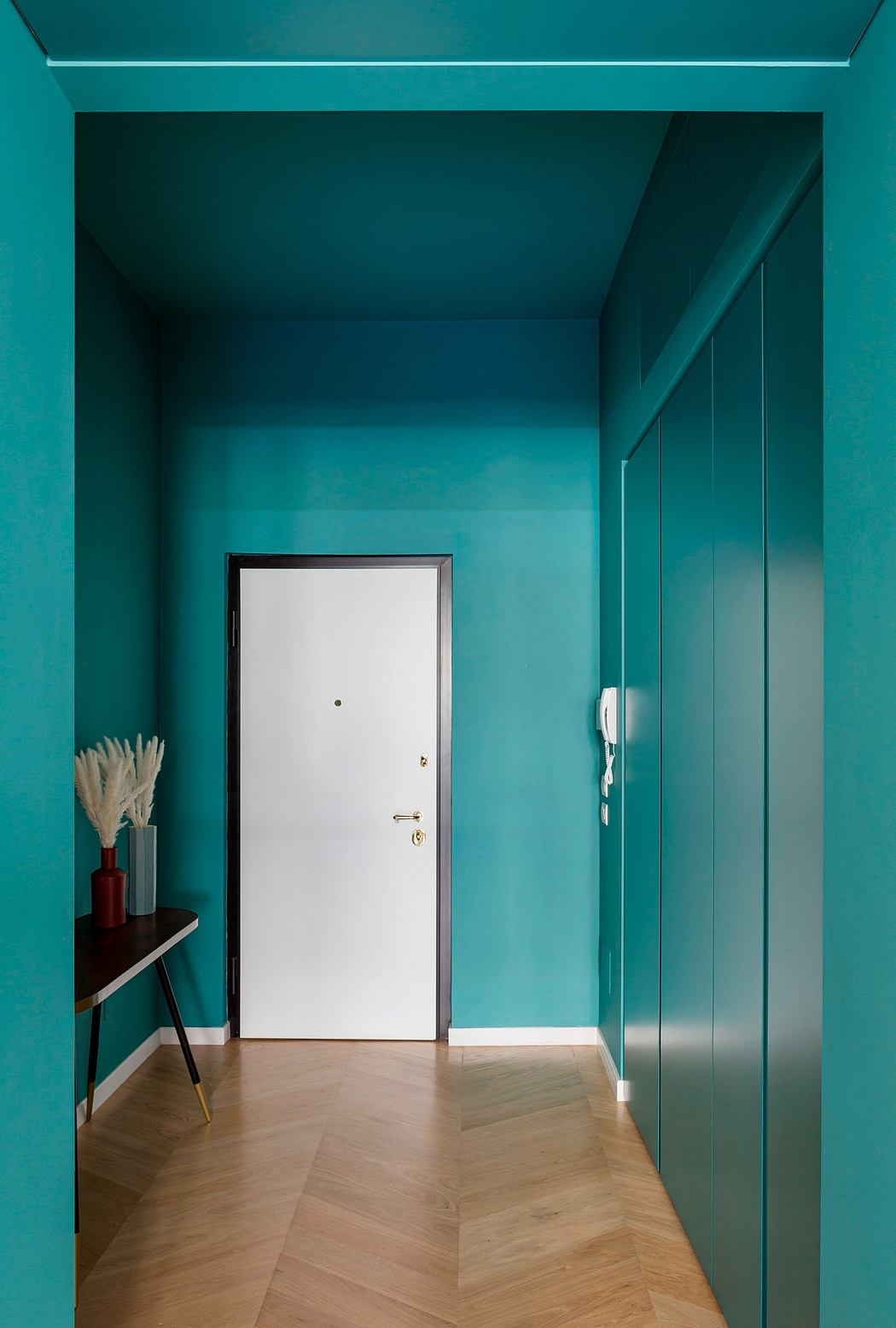 Vibrant teal walls, white door, and wooden flooring create a striking entryway design.