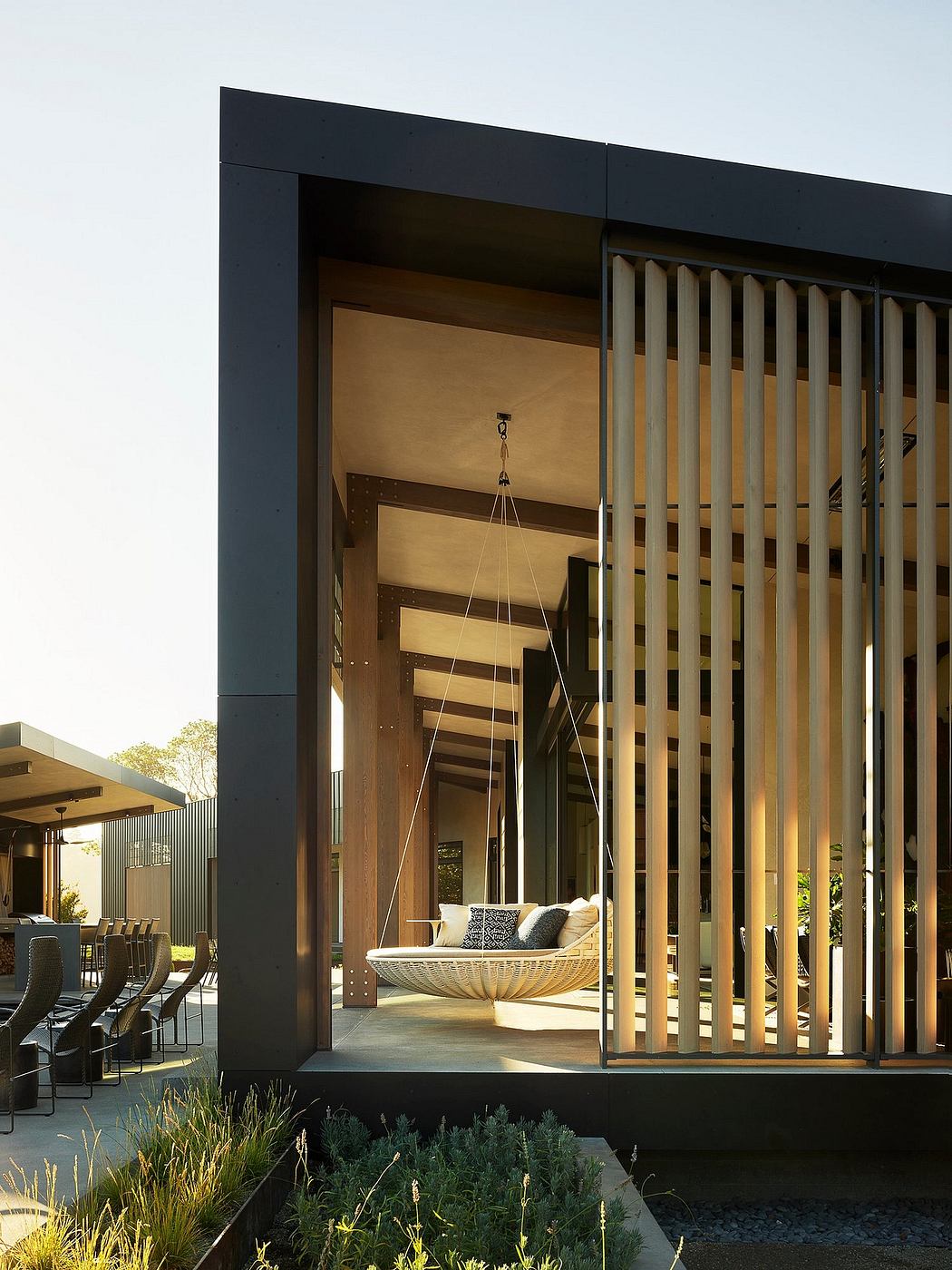 Sleek modern exterior with wooden slats, suspended daybed, and lush landscaping.