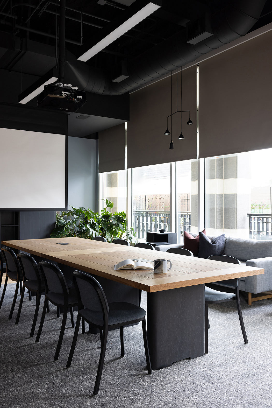 Sleek modern office space with large wooden table, black chairs, and lush greenery.