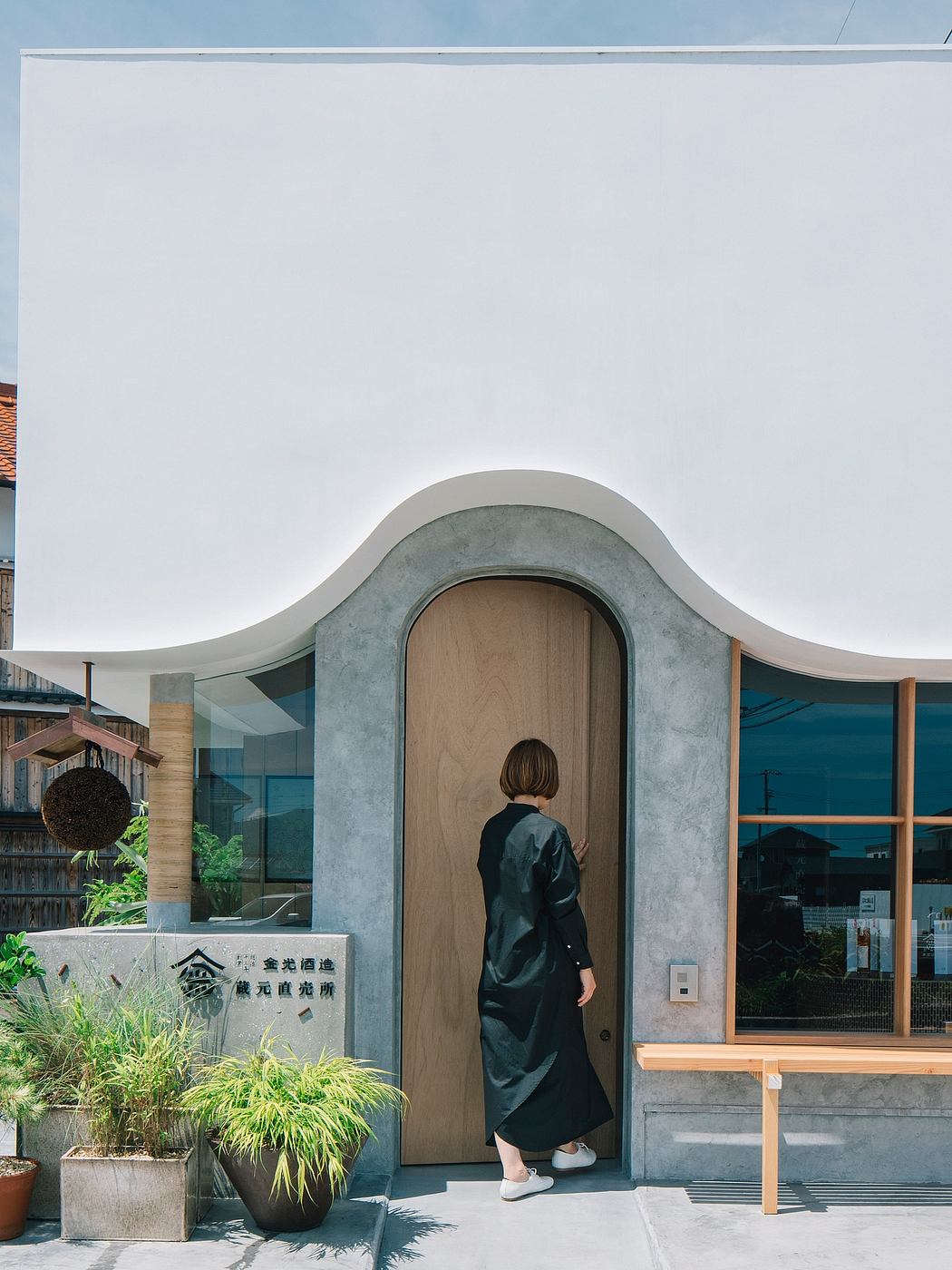 Curved concrete facade frames wooden entry door, minimalist exterior design.