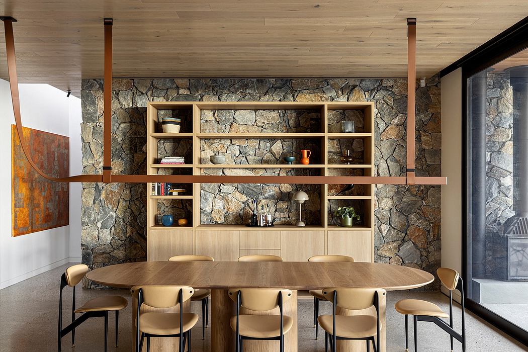 A cozy dining area with a rustic stone wall, wooden shelves, and a long oval table.