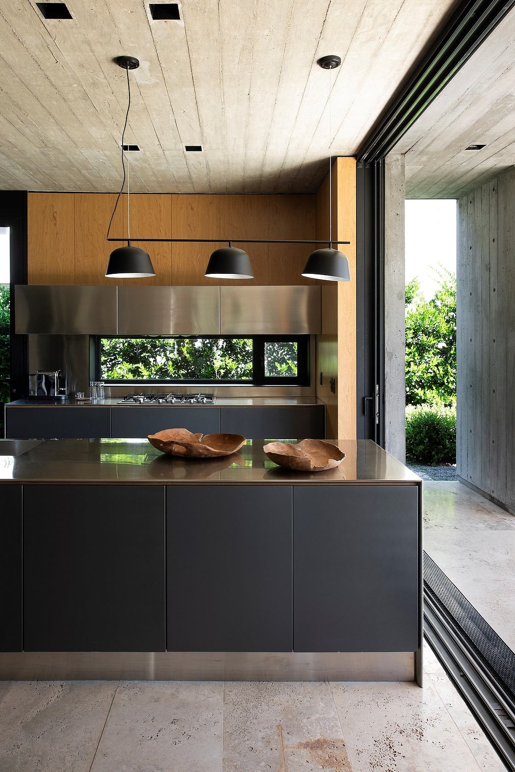 A modern kitchen with concrete walls, wooden cabinets, and sleek black pendant lights.