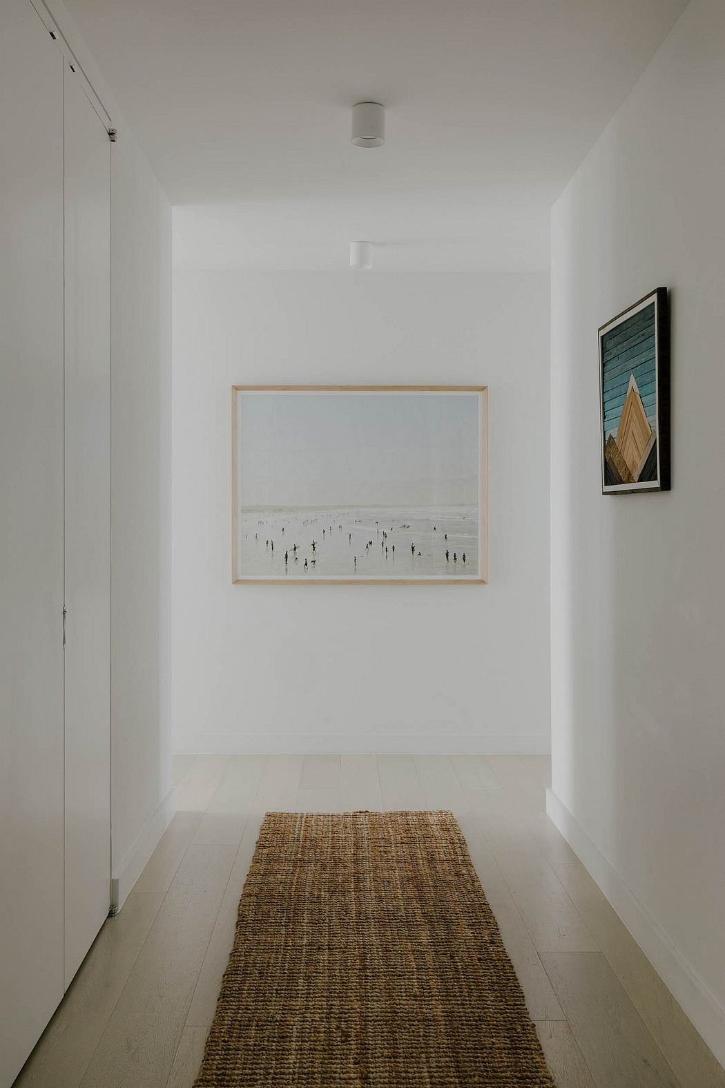 Minimal white hallway with a framed artwork and a woven rug on the hardwood floor.