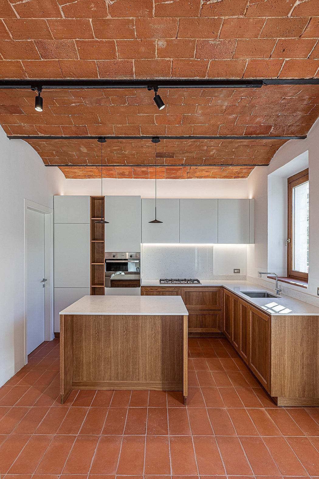 Rustic kitchen with exposed brick walls, wooden cabinetry, and a tiled floor.