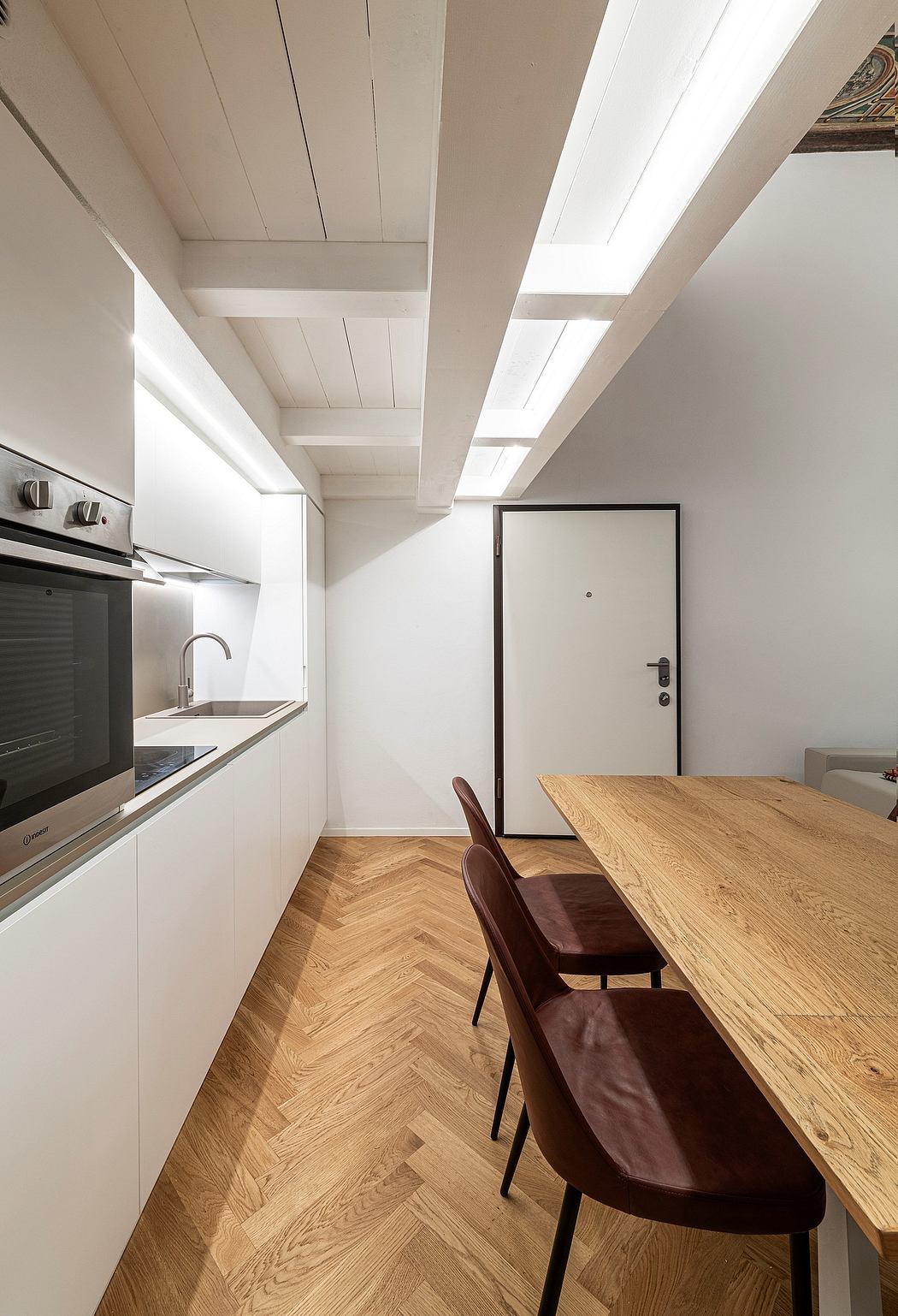 A modern, minimalist kitchen with wooden floors, white walls, and recessed lighting.