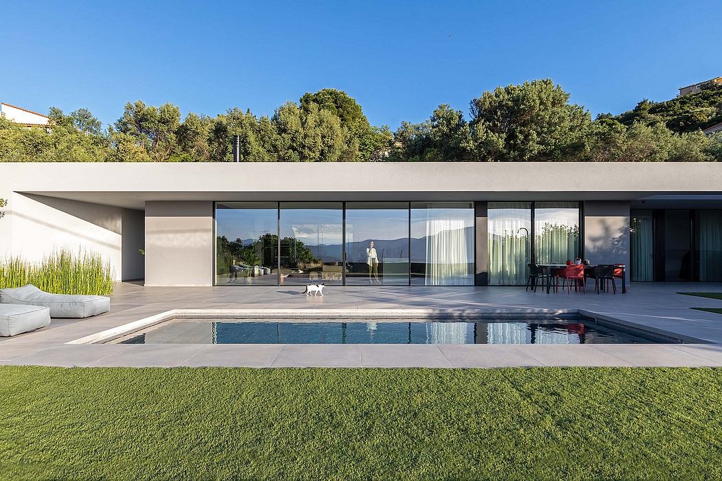 Sleek modern home with large glass windows, pool, and lush landscaping.