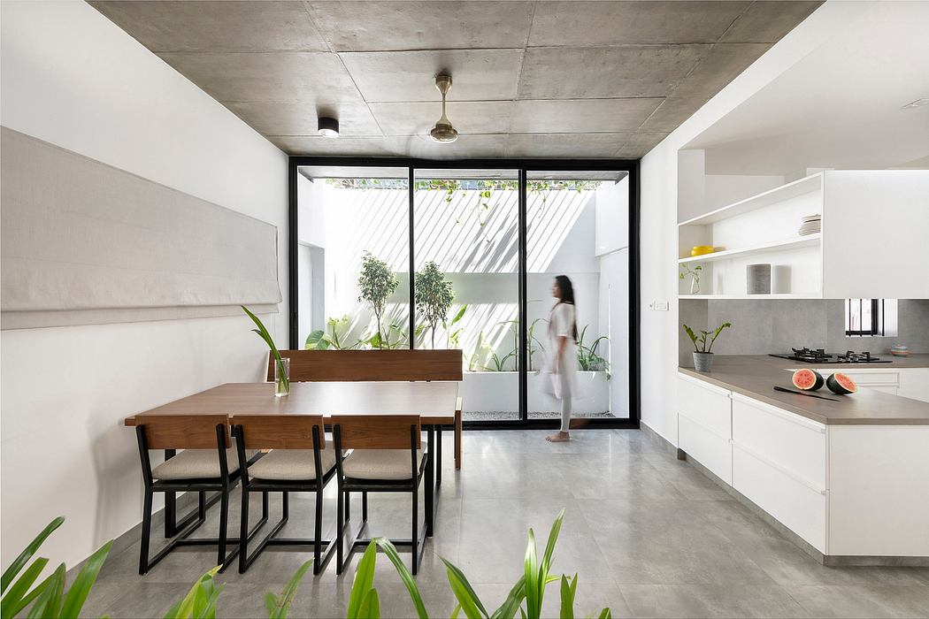 A modern, minimalist kitchen and dining area with concrete floors, large windows, and a wooden table.