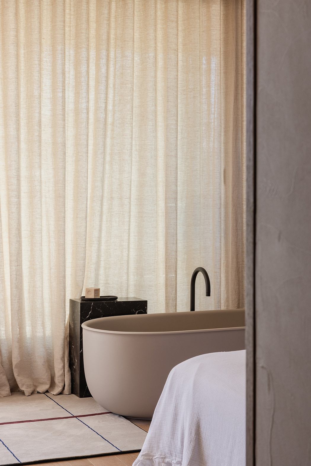 Minimalist bathroom with freestanding tub, marble vanity, and flowing curtains.