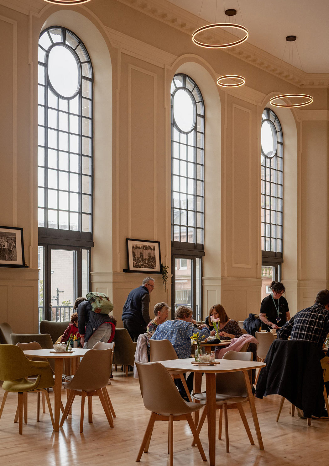 A grand, ornate interior with arched windows, circle lighting, and people dining.