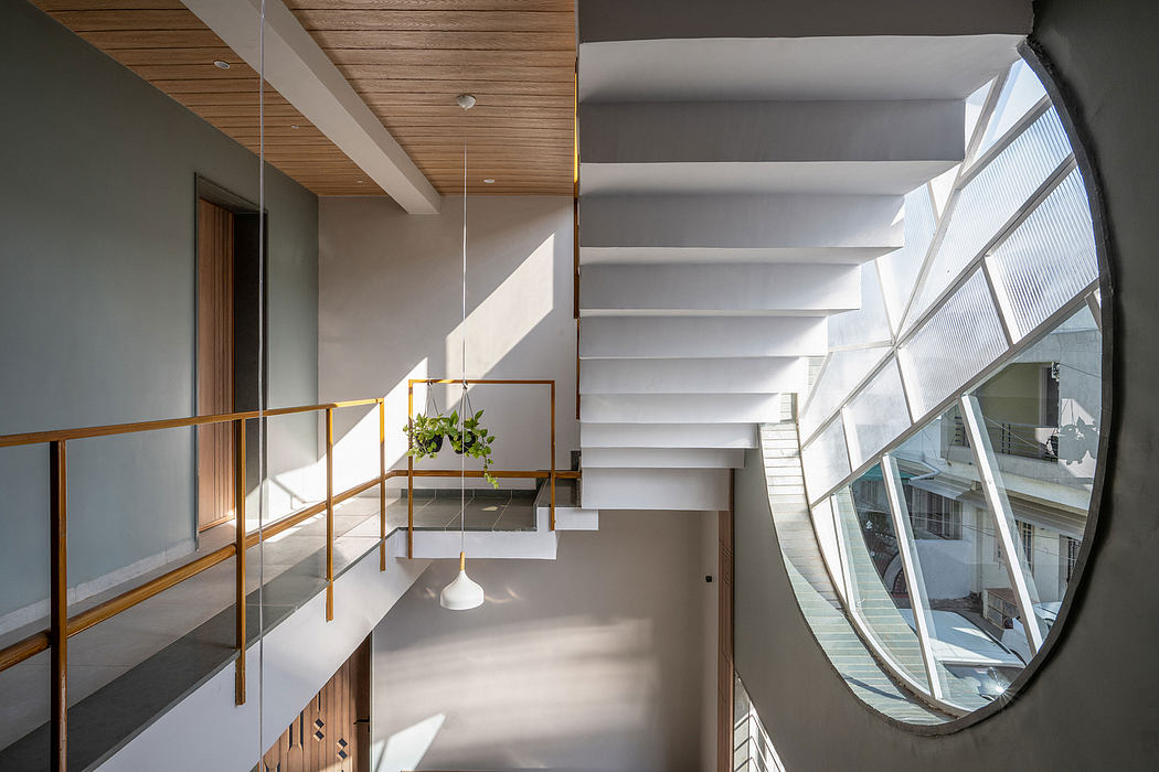 Contemporary staircase with wooden ceiling, hanging plants, and large curved window providing natural light.
