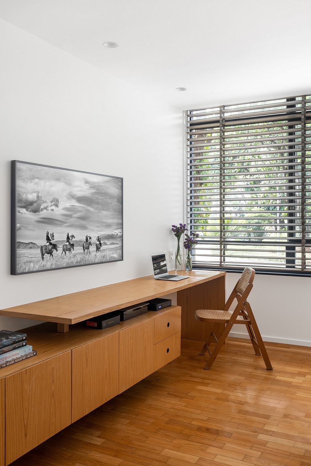 Minimalist home office with wooden cabinetry, large window, and framed artwork.