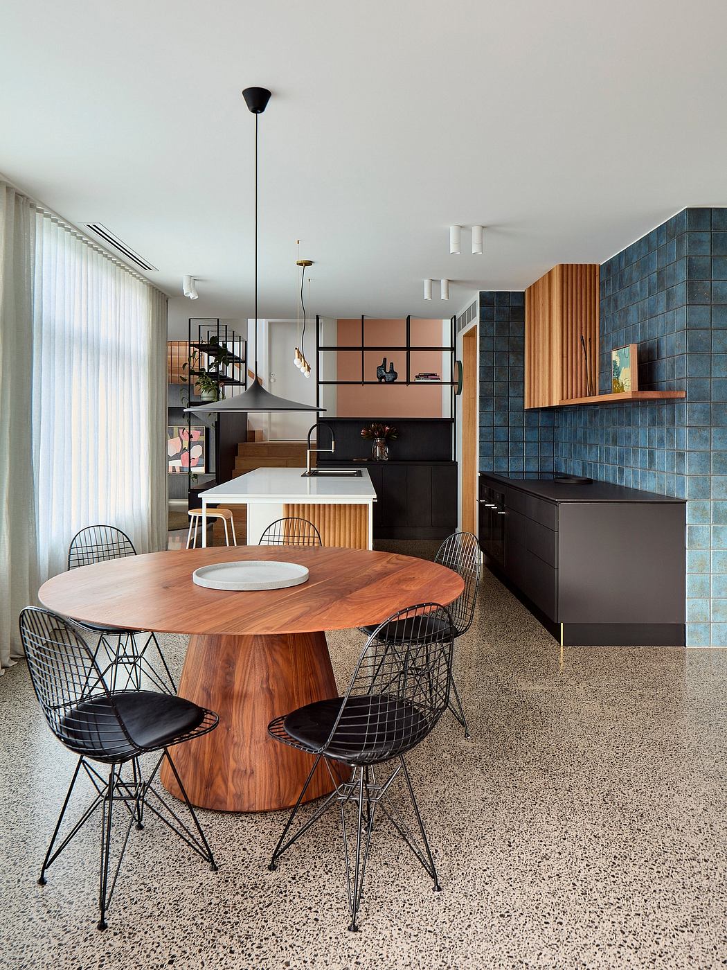 A contemporary kitchen and dining area with a sleek black and wood design, featuring a round wooden table and wire-framed chairs.