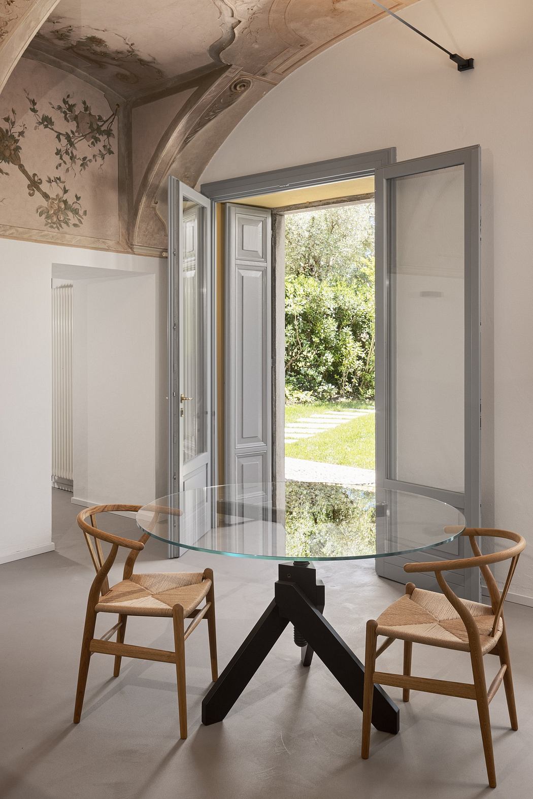 A glass-topped dining table with wooden chairs in a grand, arched room with ornate wall decor.