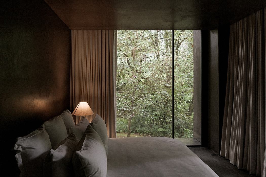 Cozy, dimly lit bedroom with large window overlooking lush, verdant woodland.