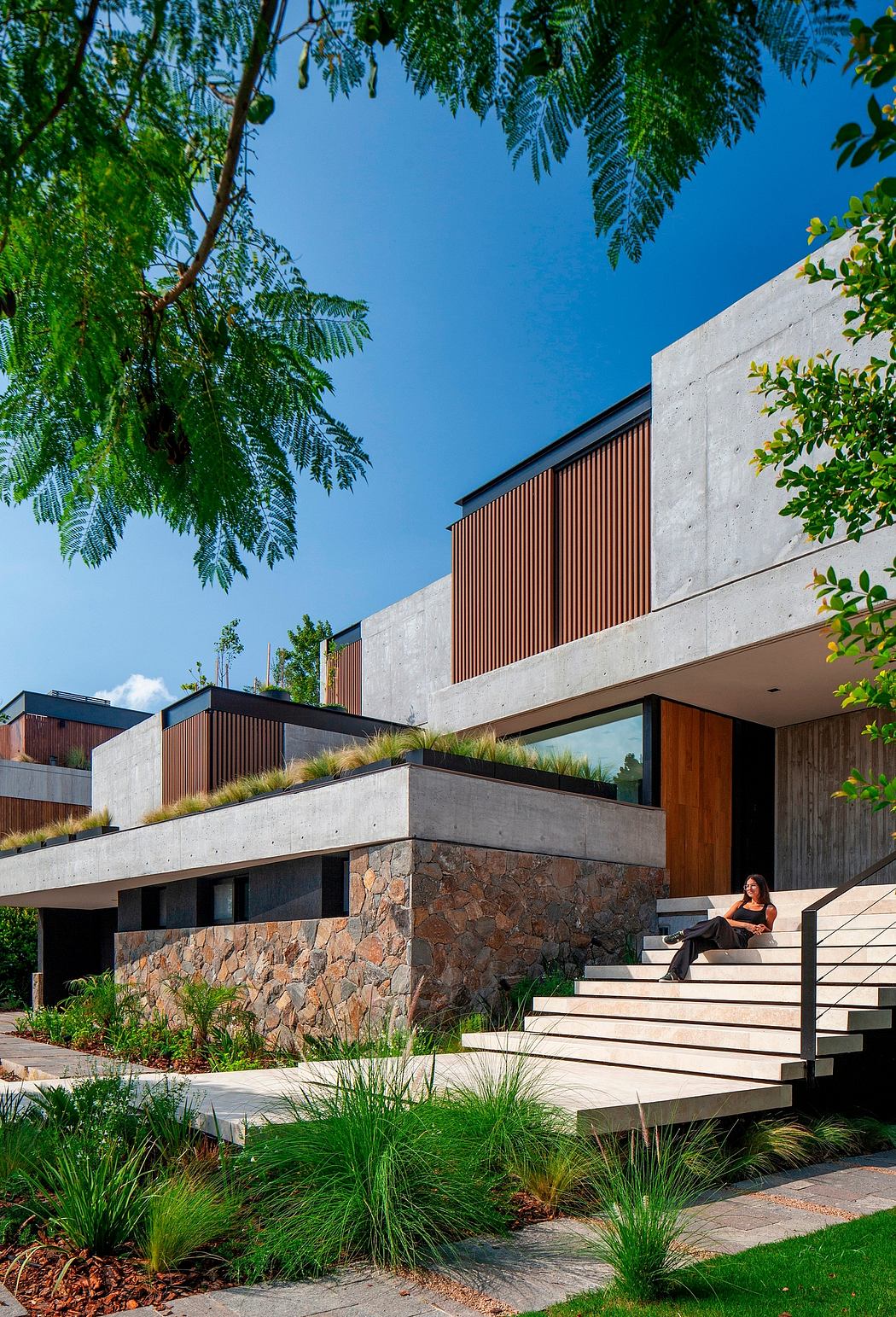 Modern architectural design showcases concrete, wood, and stone elements, accentuated by lush greenery.