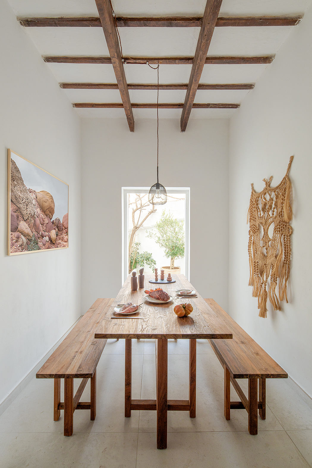 Rustic wooden ceiling beams, textured dining table, and macrame wall decor create a cozy, natural ambiance.
