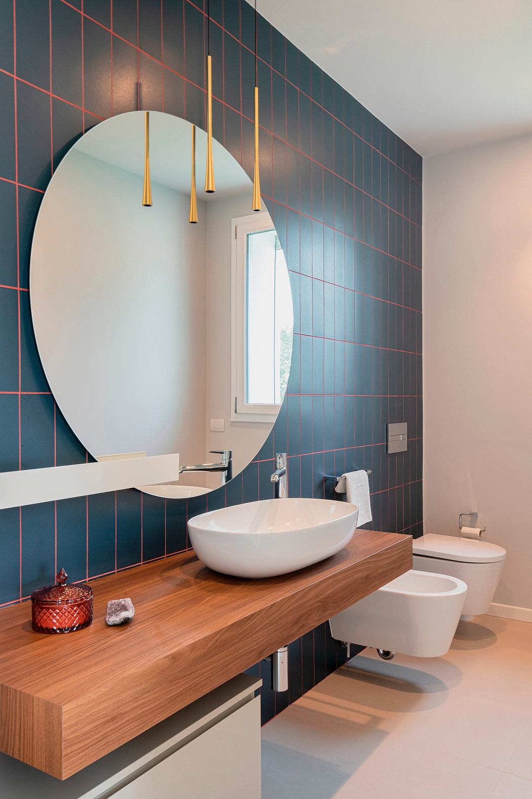 A luxurious modern bathroom with a sleek oval mirror, golden sconces, and a wooden vanity.