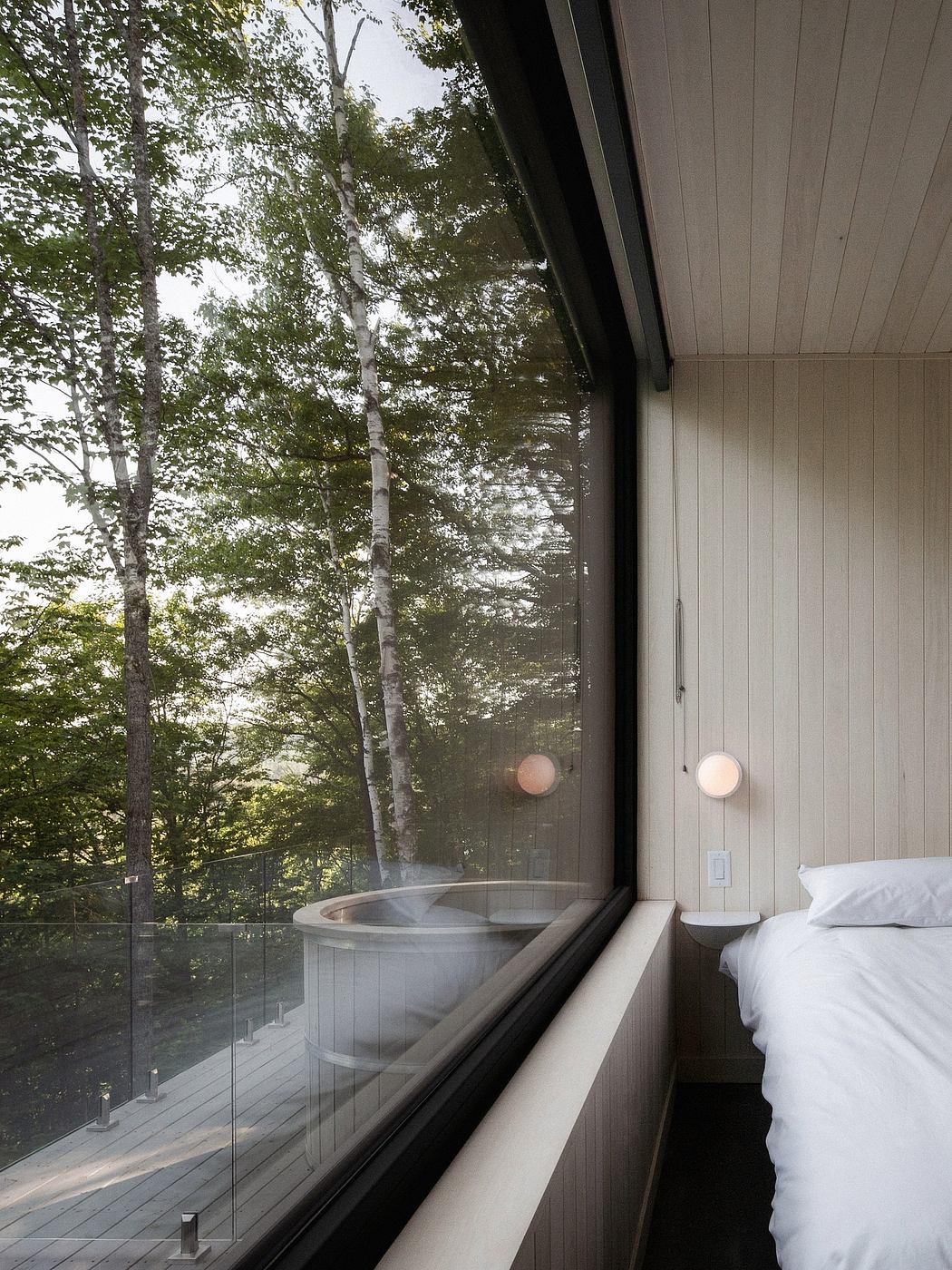 A cozy indoor hot tub with glass walls overlooking a lush forest outside.