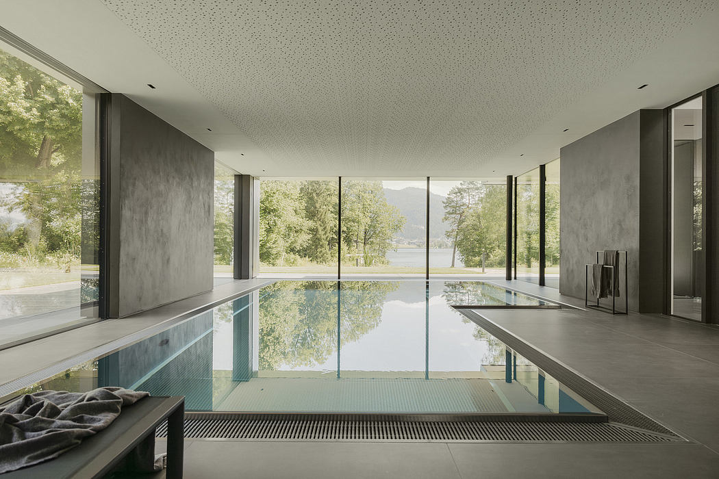 An interior with a large glass wall overlooking a tranquil pool and lush forest landscape.