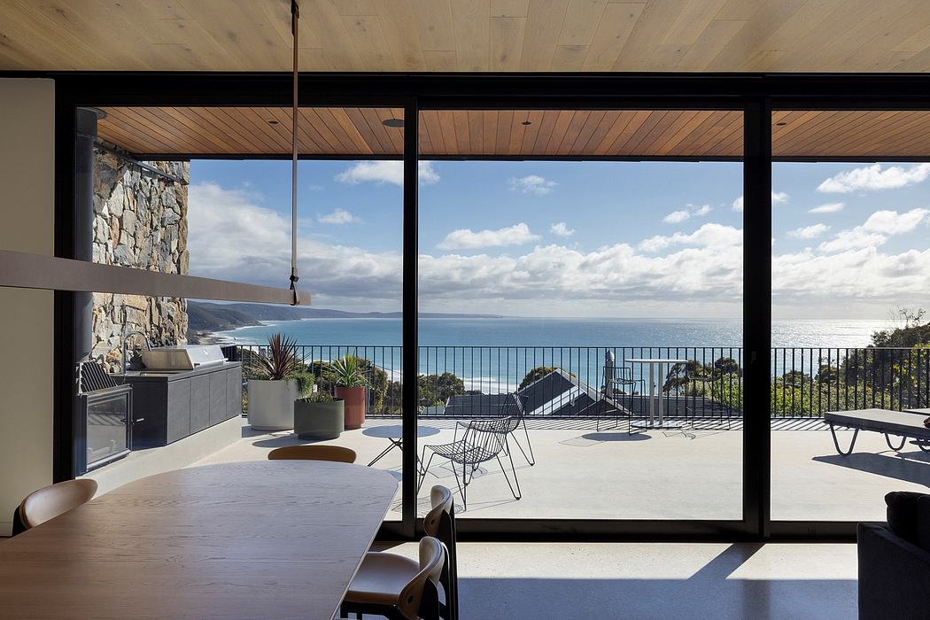 Expansive glass walls frame a breathtaking ocean vista, with a sleek outdoor kitchen and seating area.