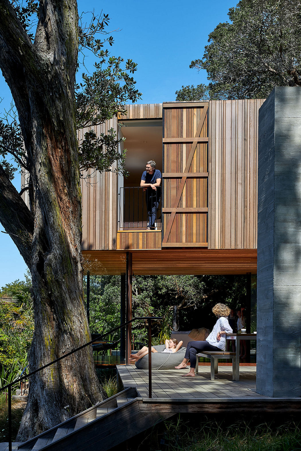 A modern wooden structure elevated on stilts, with a partially covered porch and lounge area.