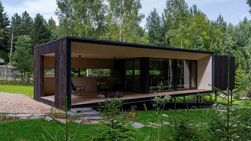 A modern cabin-like structure with a large covered porch set in a lush forest environment.