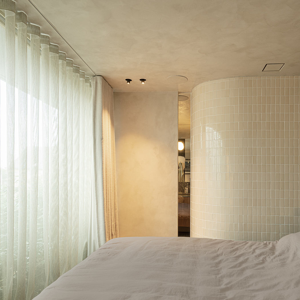 A cozy bedroom with a tiled bathroom alcove, illuminated by warm lighting and curtains.